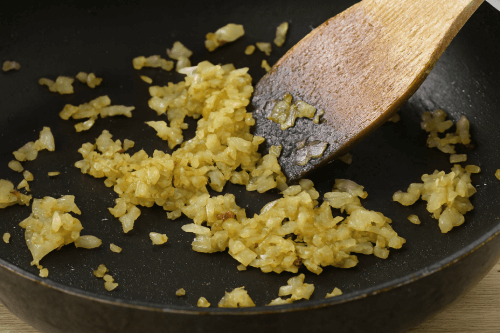 Sautéing finely chopped onions and garlic in olive oil in a large pan until translucent, the first step in building flavor for a hearty homemade sauce.