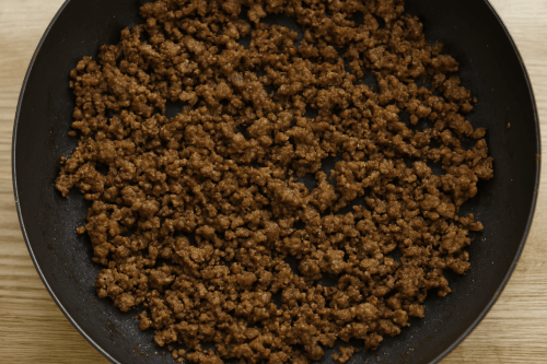"Seasoned ground meat in a pan with salt, pepper, basil, oregano, onion powder, paprika, and a pinch of sugar, gently stirred to blend flavors during the sauce-making process.