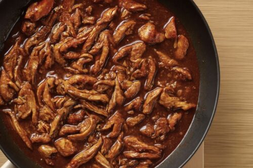 Shredded cooked chicken mixed into spicy taco sauce in a skillet for flavorful chicken taco filling