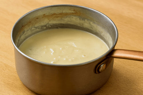 Classic-Beef-Lasagna-2 Creamy bechamel sauce being whisked in saucepan with milk, butter, flour and parmesan for lasagna