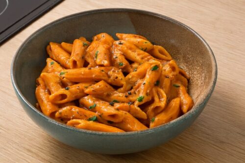 Cooked penne pasta tossed in creamy tomato sauce, coated evenly with a silky finish and specks of pepper.