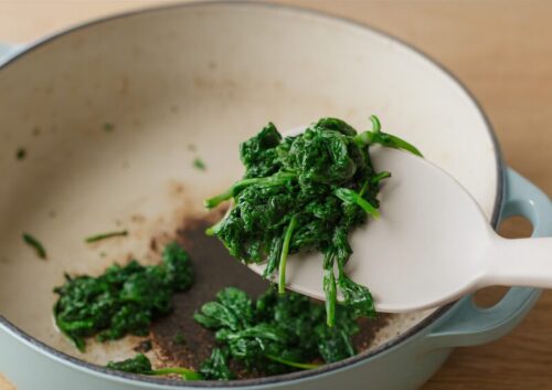Fresh spinach sautéing in olive oil in a pan with light steam rising