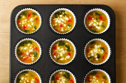 Egg mixture poured into muffin cups topped with red bell pepper and feta