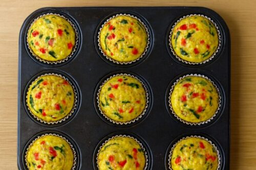 Muffin tray baking in oven with golden edges forming on spinach egg muffins