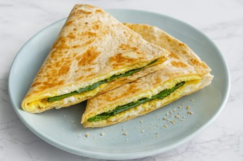 Egg-Quesadilla-5 Sliced spinach and egg breakfast quesadilla wedges served on light blue plate, filled with melted cheese and golden tortilla.