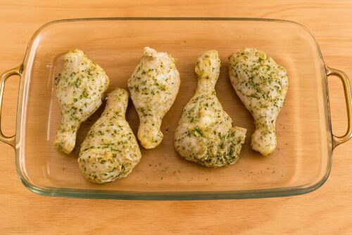 Garlic-Herb-Roasted-Chicken-3 Marinated chicken arranged in a baking dish with herbs sprinkled on top before placing it in a preheated oven for roasting at 200°C.