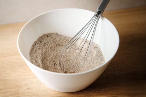 Grinding rolled oats into oat flour and mixing with baking powder, baking soda, salt, and cinnamon in a bowl.