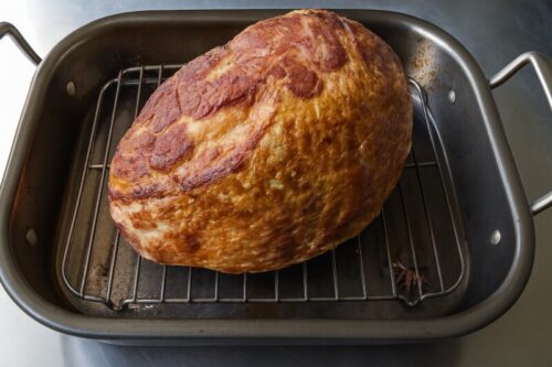 Raw 7-pound ham placed on rack inside roasting pan for baking preparation