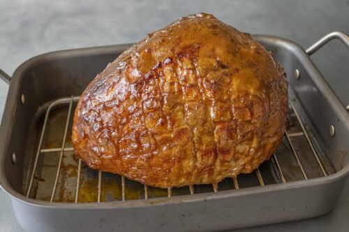 Glaze being brushed generously over ham after first bake for golden caramelized finish