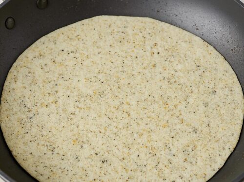 Quesadilla-3 Raw tortilla placed over cooked spinach and cheese omelette in pan, showing layering step for egg breakfast quesadilla.