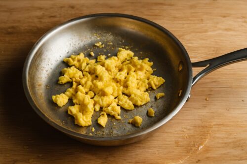 Scrambled eggs cooking in a non-stick pan with butter, gently stirred with spatula.
