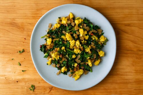 Scrambled eggs mixed with cooked spinach and mushrooms in pan, ready to serve.