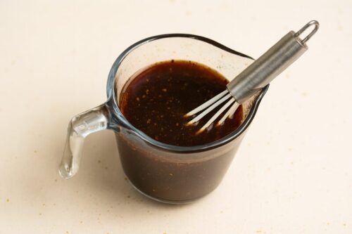 Bowl of mixed teriyaki sauce ingredients including soy sauce, garlic, ginger, and cornstarch on a kitchen counter.