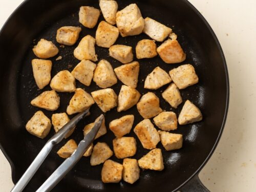 Boneless chicken pieces cooking in a pan with a light golden sear, showing early stage of stir-fry.