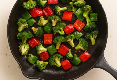 Chopped vegetables like broccoli and bell peppers being stir-fried in a pan with a little oil.