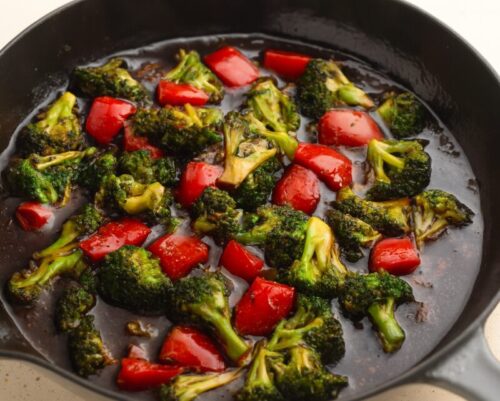 Teriyaki sauce poured over cooked vegetables in a pan, simmering and starting to thicken.