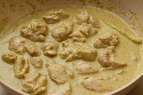 Chicken pieces stirred into green curry base for even coating and flavor absorption