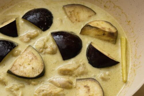 Chicken stock, water, and coconut milk poured into curry base with aubergine simmering until slightly softened