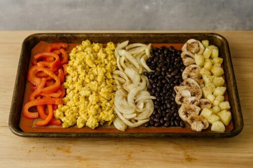 Veggie-Breakfast-Burrito-Bowl-2 Bell peppers, tofu, onions, black beans, mushrooms and potatoes spread on baking sheet with paprika, chili powder, and garlic seasoning sprayed with olive oil for roasting