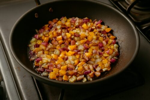 Onions and bell peppers sautéing in skillet until soft and slightly translucent