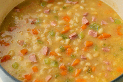 Adding chicken stock, beans, and ham into the pot.